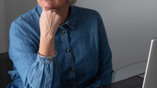 A cropped image of a woman resting her chin on her closed hand as she sits at a computer