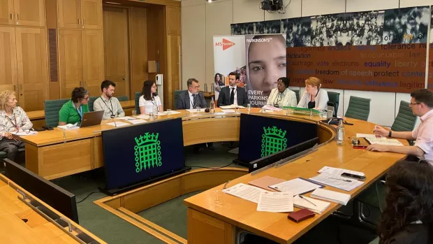 People sat round a wooden horseshoe shaped table in parliament. Behind them are banners for Parkinson's UK and MS Society