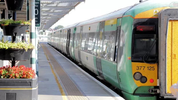 A green and yellow train is pulled up on a platform, there are baskets of flowers in the platform which is open air. 