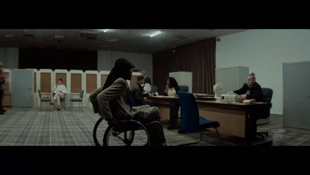 A man in a wheelchair in a job centre wheels towards a woman sat at a desk