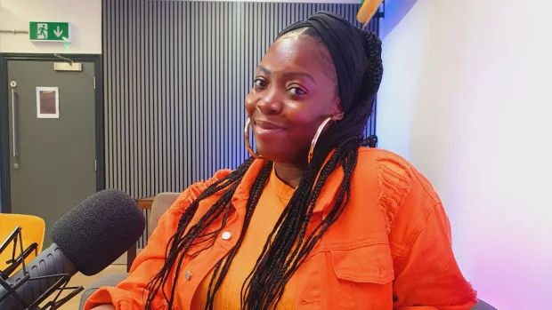 Elisha sits in front of a microphone wearing an orange top.