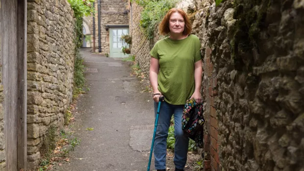 Bethen leans against a wall, using a walking stick.