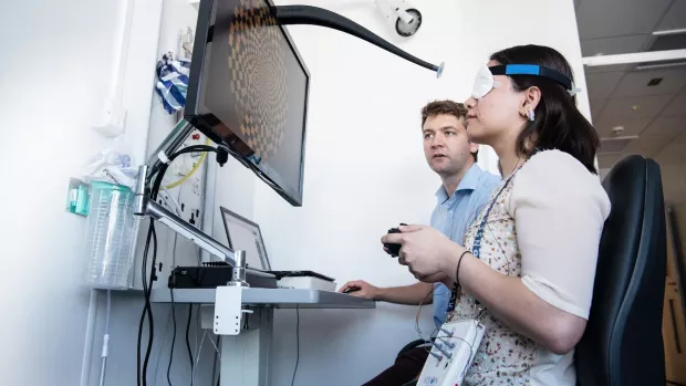 Dr Nick Cunniffee sits at a computer with a research participant who is operating a device in front of a monitor