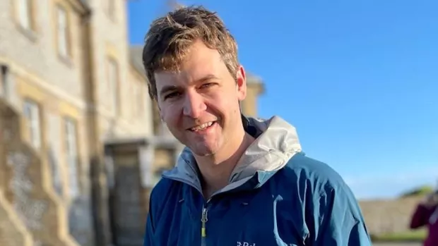Dr Nick Cunniffe wears a blue hooded jacket and has short light-brown hair