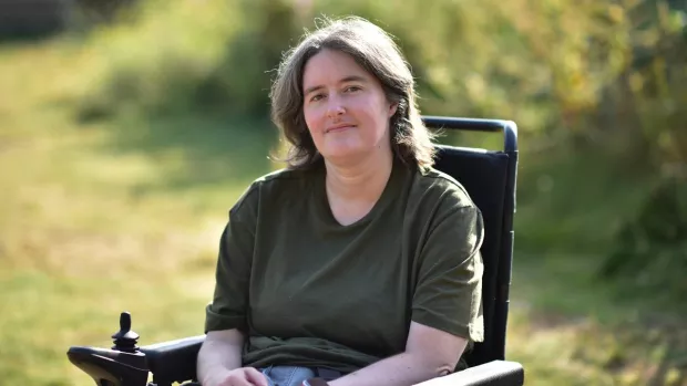 Karine is shown using her wheelchair, sitting in a grassy area.