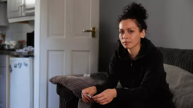 A person in a dark hooded top with long dark hair tied up on top of their head stares confidently into the camera