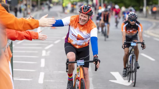 A cyclist in an orange MS cycling shirt high-fives supporters, also wearing orange