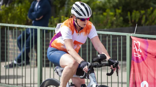 A cyclist on a bike wearing an orange and white MS Society cycling shirt.