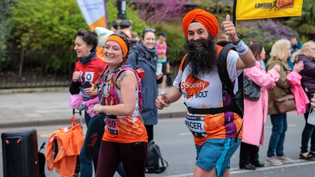 Two runners in MS Society t-shirts smile at the camera as they jog, one gives a thumbs-up