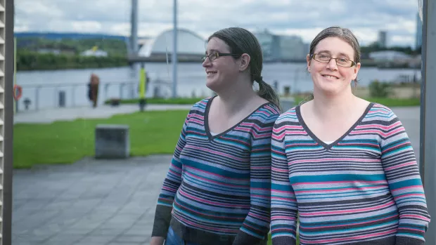 A woman in a striped top stands outside next to a mirror