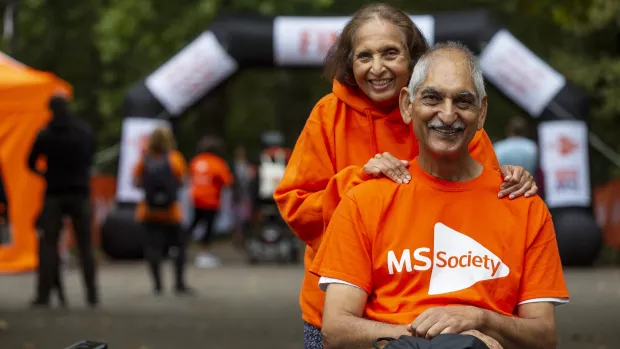 A woman has her hands on the shoulders of a person in a wheelchair - both wearing MS Society t-shirts