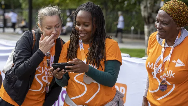  Three people in MS Walk t-shirts looking at a phone