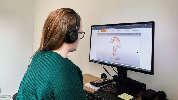 A woman with MS wears headphones and works on a computer