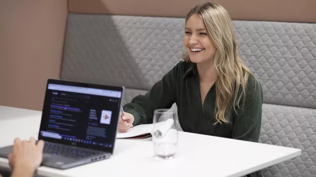 A woman smiling while writing in a notepad in an office