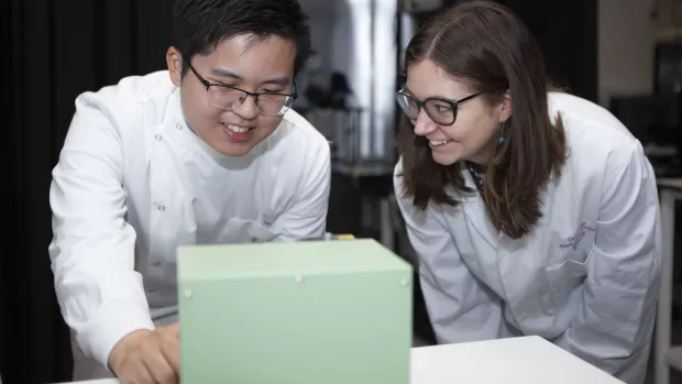 Two researchers in lab coats working together in a lab.