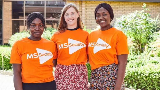 Three volunteers wearing MS Society t-shirts, standing outside