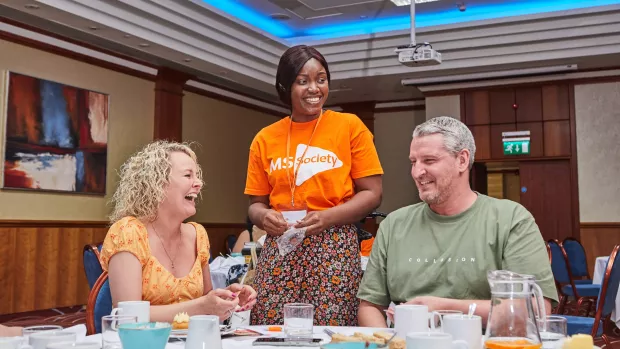 A person in an MS Society t-shirt and local group members chat at a group social event 