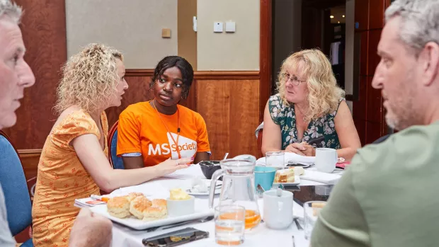 A group of people sitting round a table sharing their MS stories