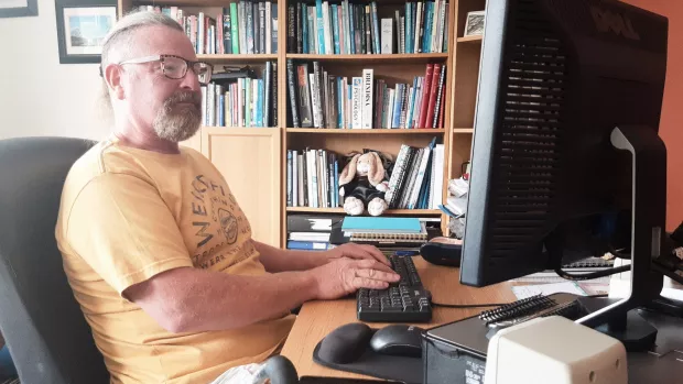 Person sitting at a desk looking at a monitor and typing on a keyboard