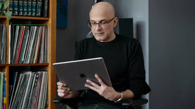 A man in a black top looks at an iPad in his living room
