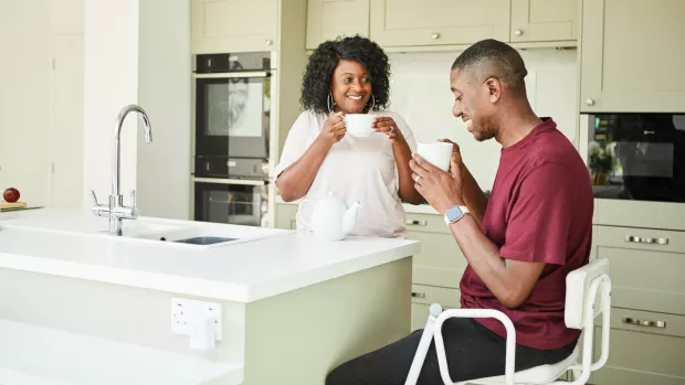 A couple drinking from mugs in a kitchen 