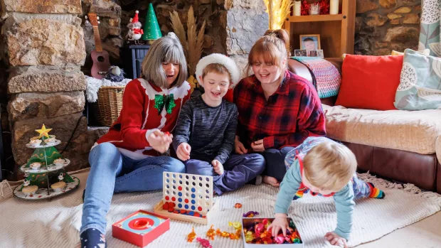 A family are sat on the floor playing games surrounded by Christmas decorations