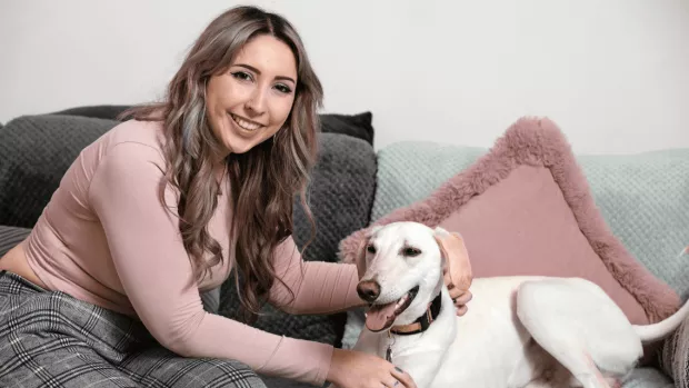 Person sitting on a sofa with their dog, smiling.