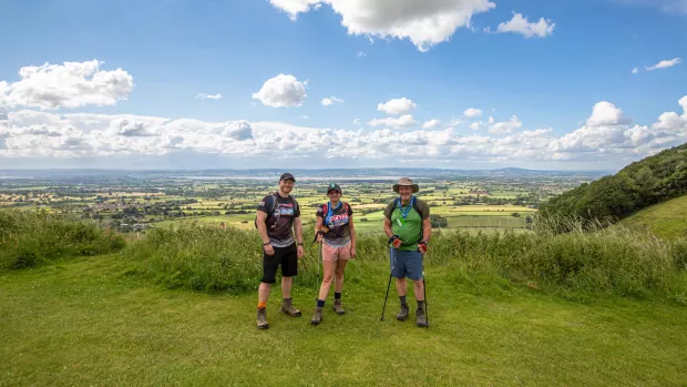 Three people in shorts stand on a grassy hill with the Kent Downs stretching out in the background