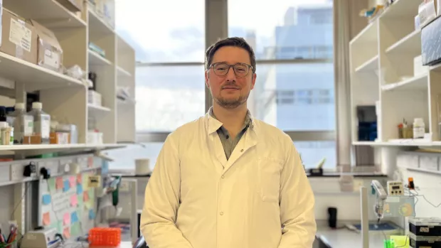 Researcher Cory Willis standing in his lab, wearing a white coat