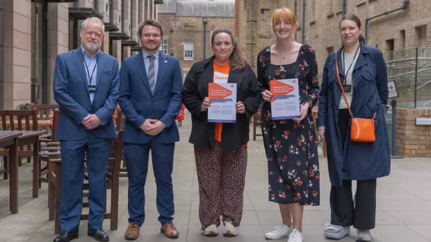 A group of five people stood outside parliament, two of them holding copies of the MS Society 2024 election manifesto.