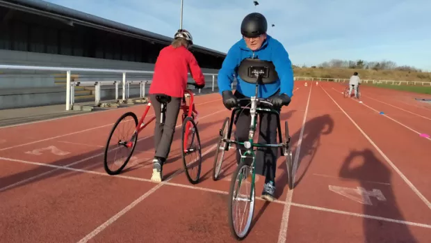 Two people running using wheeled frames on a sports track