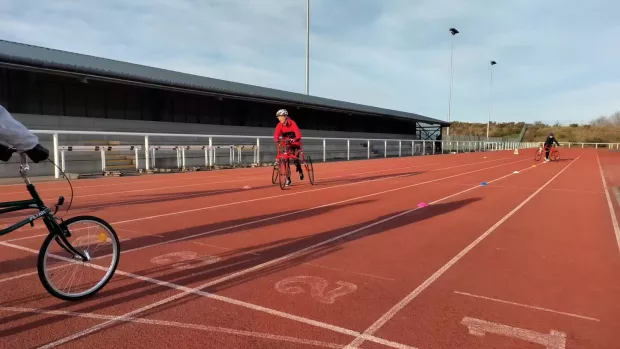A red sports track with people running using wheeled frames