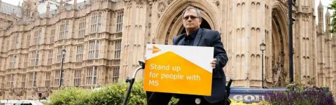 a man holding a MS campaign placard outside Westminster