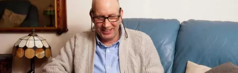 Photo: a man sits on a sofa smiling as he surfs the net