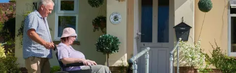 Photo: a man pushing a woman in a wheelchair outside a house