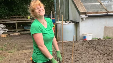 Fran wearing gardening gloves and t-shirt smiling in her garden 