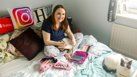Photo: Hannah sitting on her bed writing her bullet journal.