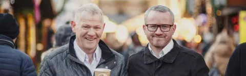 Two men standing in the street holding coffees smiling 