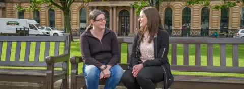Two women sitting on a bench chatting in Glasgow