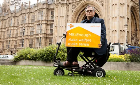 Photo shows man in mobility scooter outside Westminster holding a sign that says Make welfare make sense