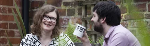 Woman smiles at man drinking coffee outside
