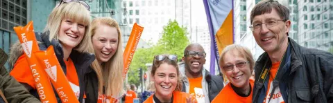 Photo shows a group of MS Society cheerers in orange t-shirts with balloons and banners