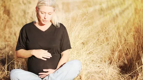 A pregnant women sitting in a wheat field with her hands on her stomach