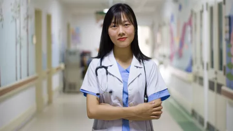 Female doctor with stethoscope stands in hospital corridor