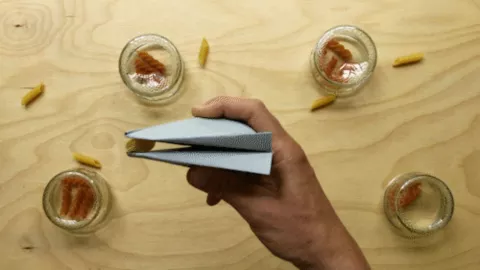 A hand holding some origami with pasta spirals in jars in the background