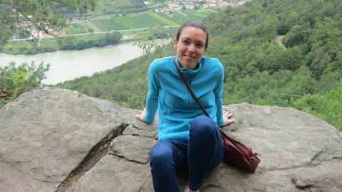 Sarah sitting on a rock smiling, with a river and countryside in the background
