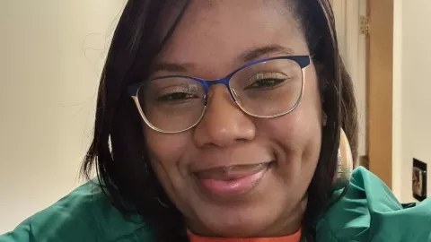 Cherelle wears glasses and a green top and is smiling to camera