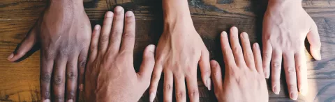 5 hands palms down on a wooden surface seen from above