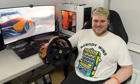 Photo of Zach sitting with his gaming computer and virtual reality racing game.
