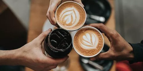 The photo shows three people holding their coffee cups together